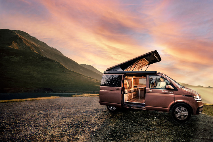 un van Woody Van devant un coucher de soleil en montagne