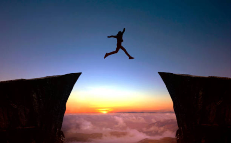 Personne sautant entre deux rochers au coucher du soleil
