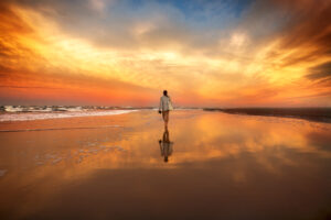 Une femme marche sur la plage au soleil couchant.