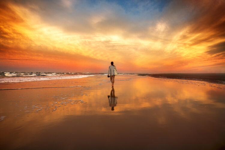 Une femme marche sur la plage au soleil couchant. 